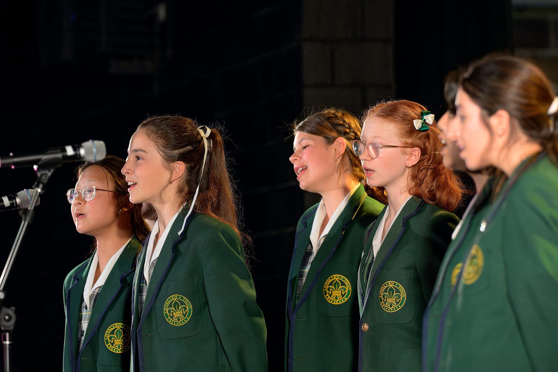 Mercedes College students in green blazers singing together on stage during a choral performance.